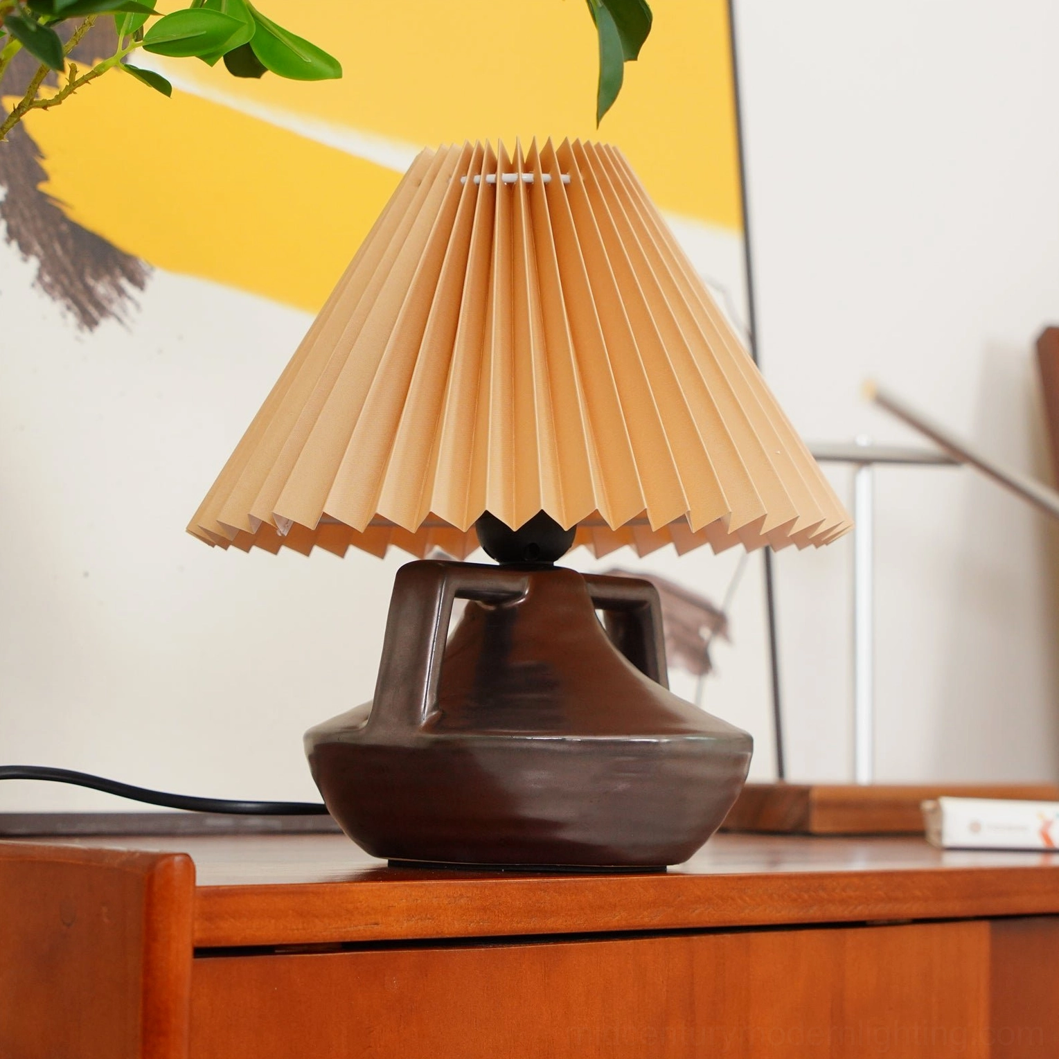 Navia table lamp positioned on wooden cabinet with wall art and green plant branches