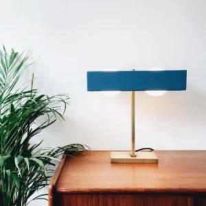 Navy blue Kernel table lamp styled on bedroom nightstand with brass hardware and green plant decor