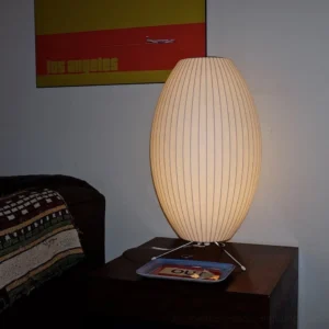 Tall oval ribbed fabric Nelson bubble lamp positioned on vintage dark wood side table in mid-century modern living room interior