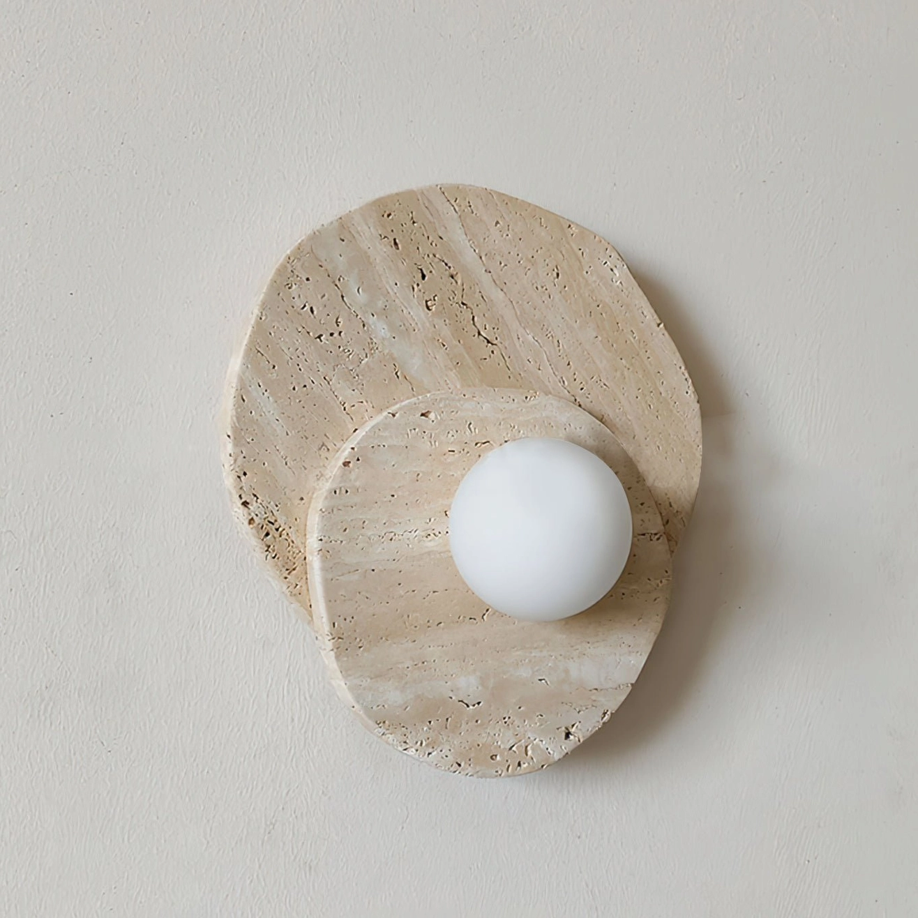 Ner travertine wall sconce with asymmetrical layered stone base and diffused frosted glass sphere on neutral background