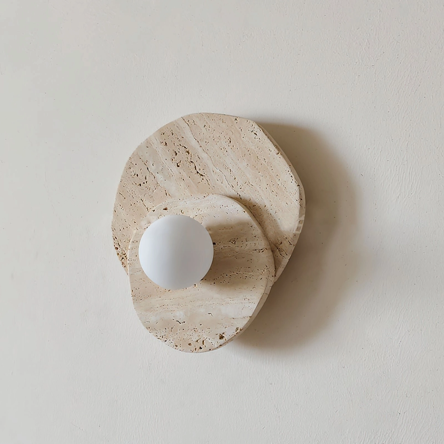 Close-up detail of Ner travertine wall light showing layered stone depth and frosted glass bulb housing against neutral wall