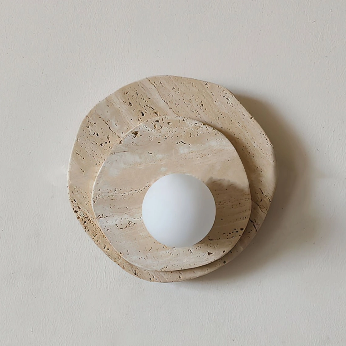 Ner travertine wall lamp with large frosted white globe showing three-layer stone construction and warm ambient illumination