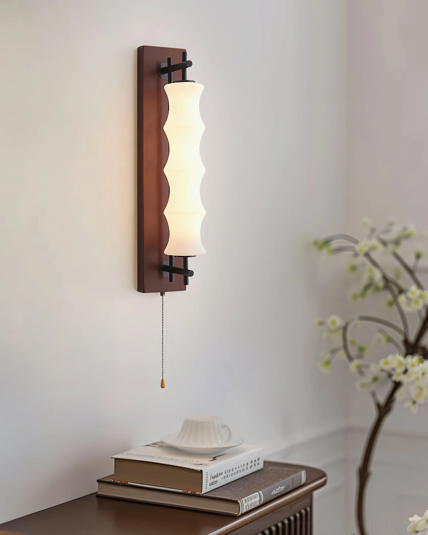 Nesta wall sconce in bedroom setting beside stacked books and floral decor, dark walnut finish with warm ambient lighting