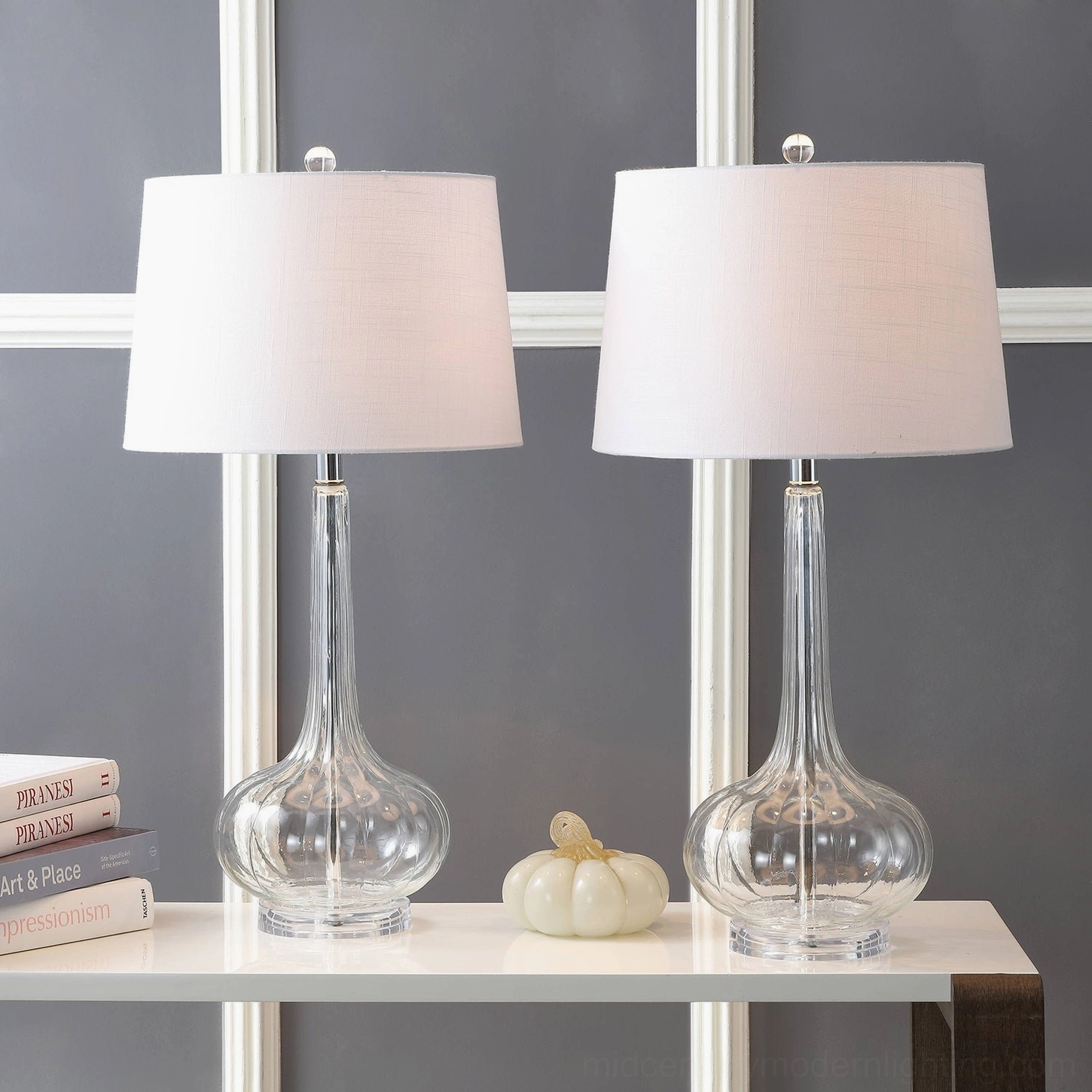 Pair of clear ceramic glass table lamps with neutral drum fabric shades on indoor shelf grey wall