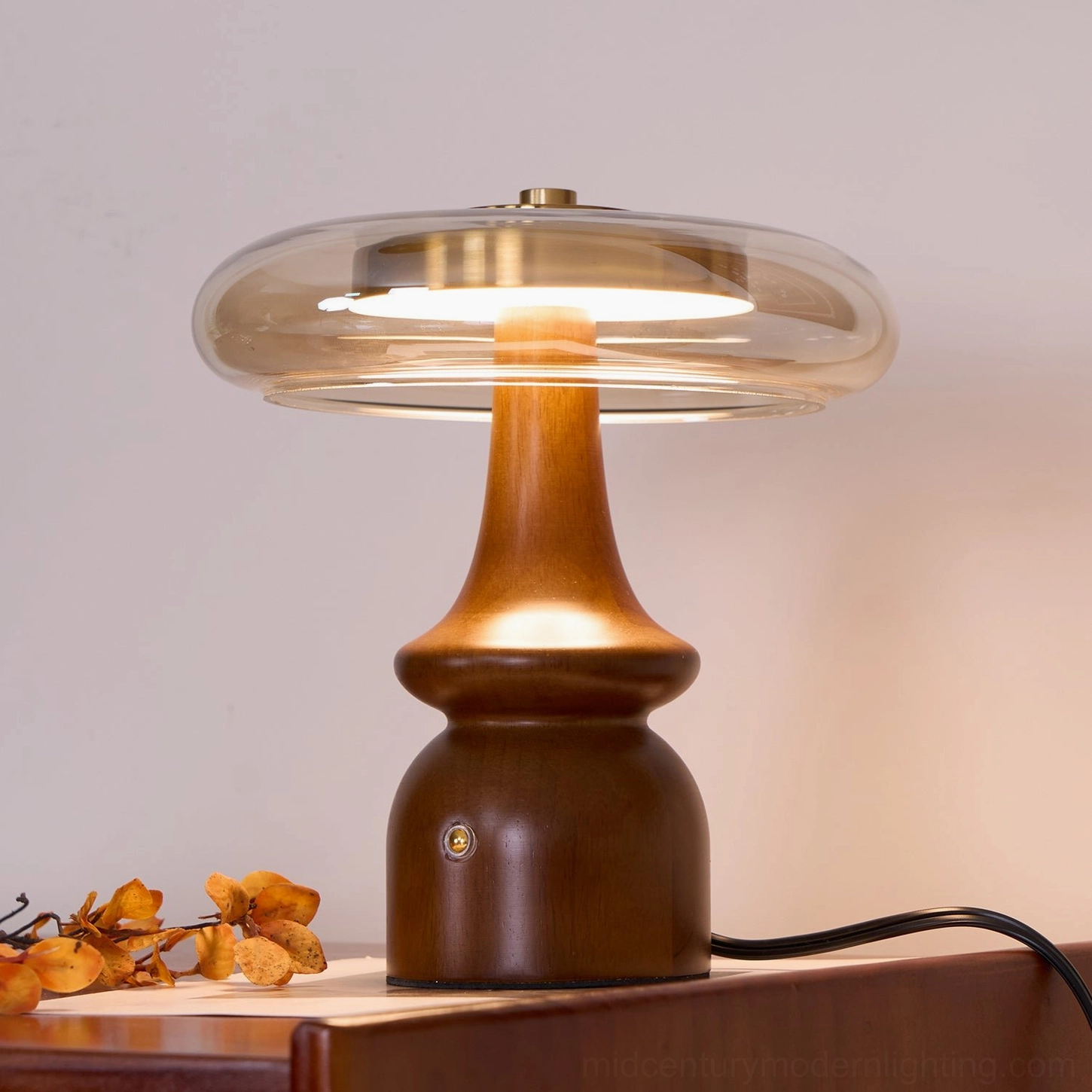 Nova mid-century table lamp right three-quarter front view lit, polished walnut finish with exposed cord on wooden surface