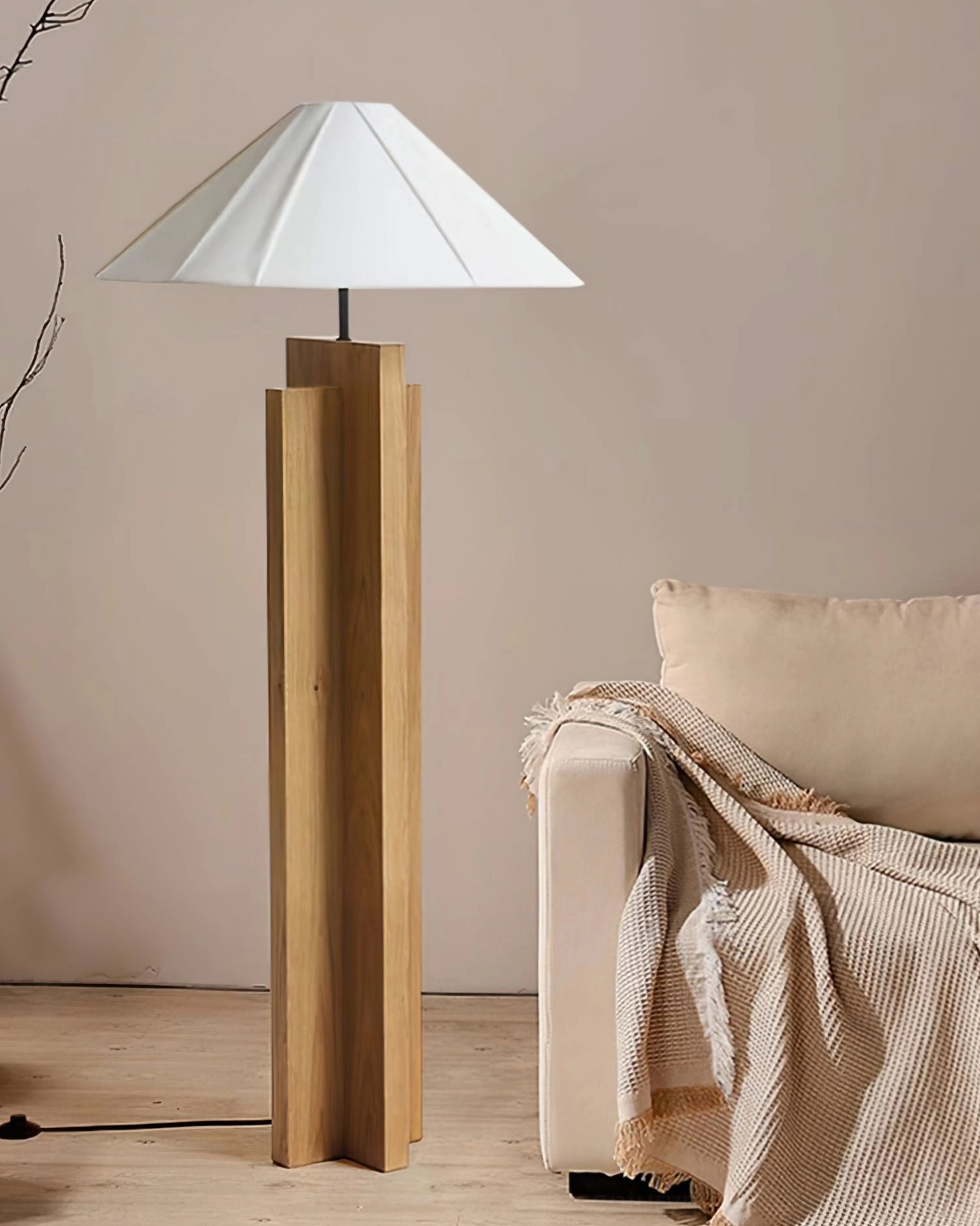 Light oak crossbase floor lamp positioned beside living room armchair with throw blanket and warm lighting