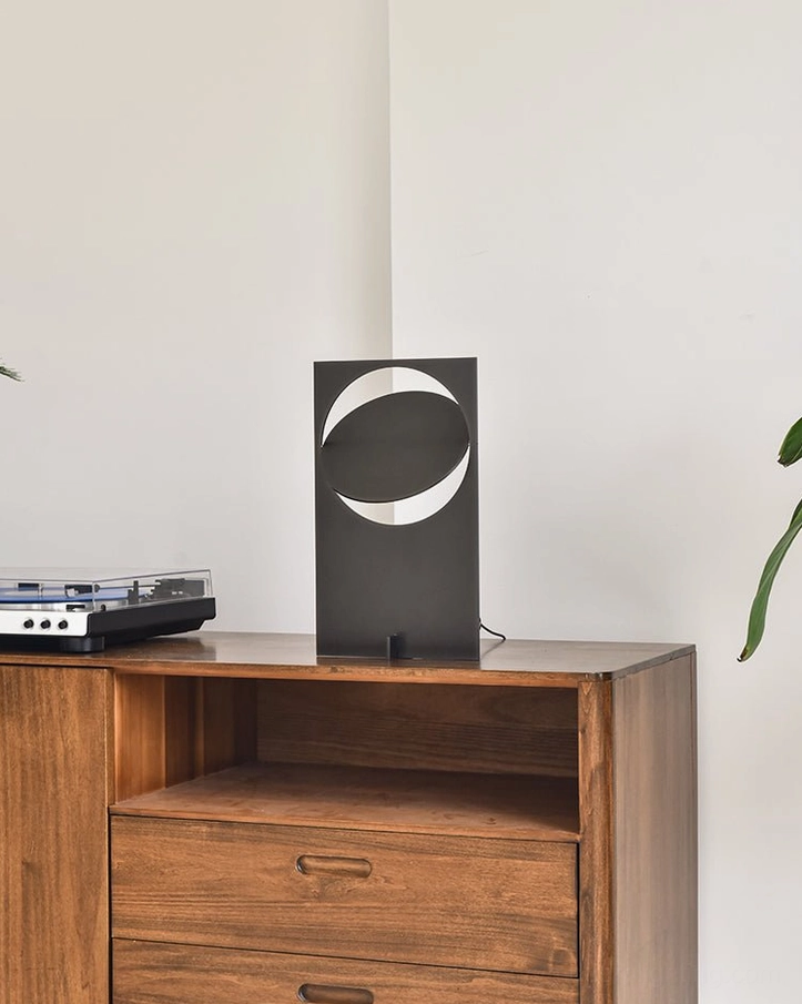 OBJ 01 matte black geometric table lamp unlit on wooden sideboard, crescent cutout silhouette, studio product photography