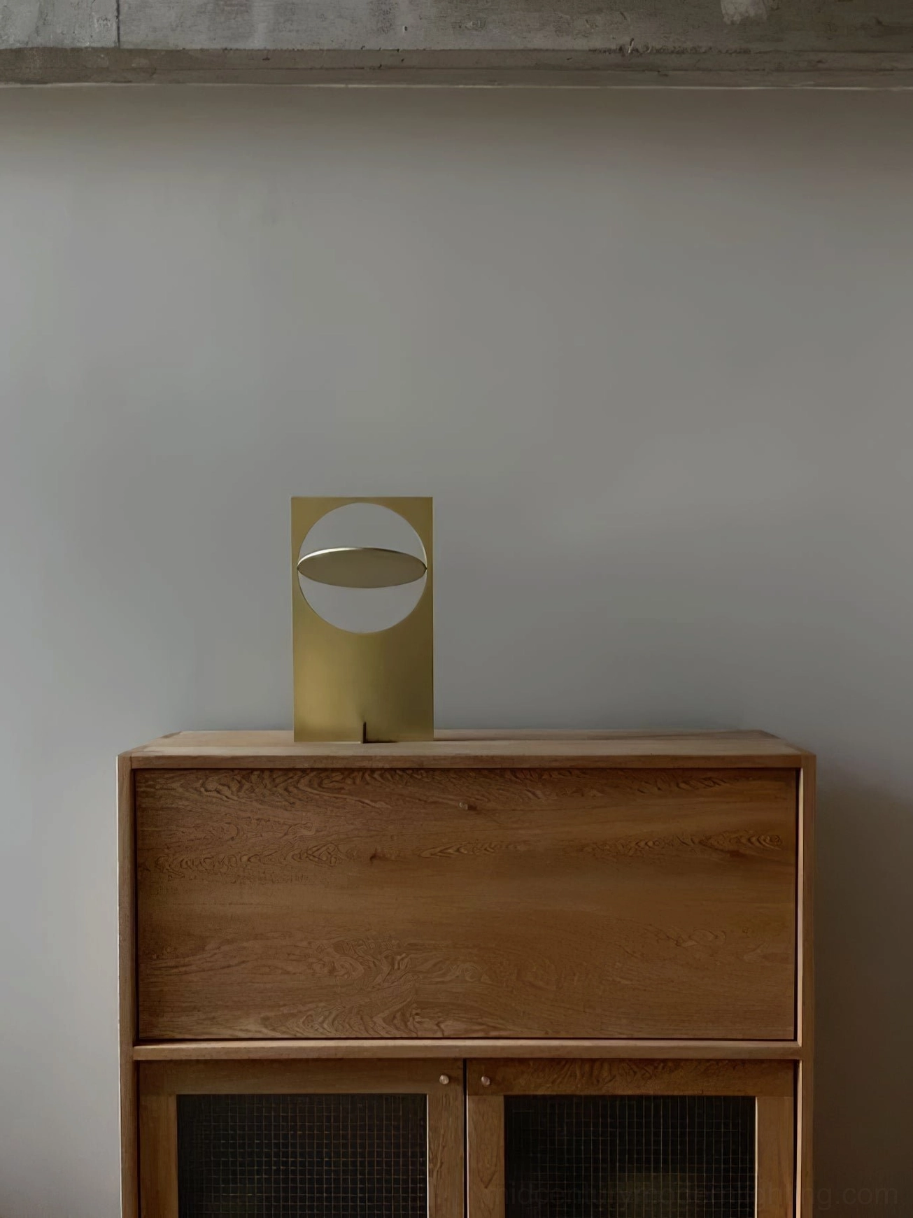 OBJ 01 compact table lamp brushed brass gold finish on wooden cabinet, front view, minimalist geometric sculptural form