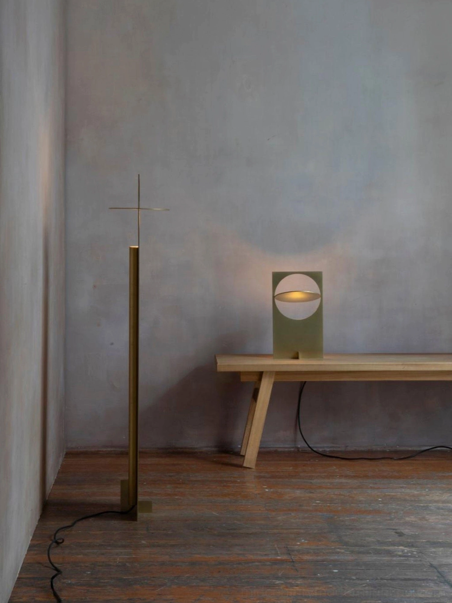 OBJ 01 brass gold table lamp lit with warm light in minimalist home interior beside wooden bench, side distant view, paired with tall floor lamp