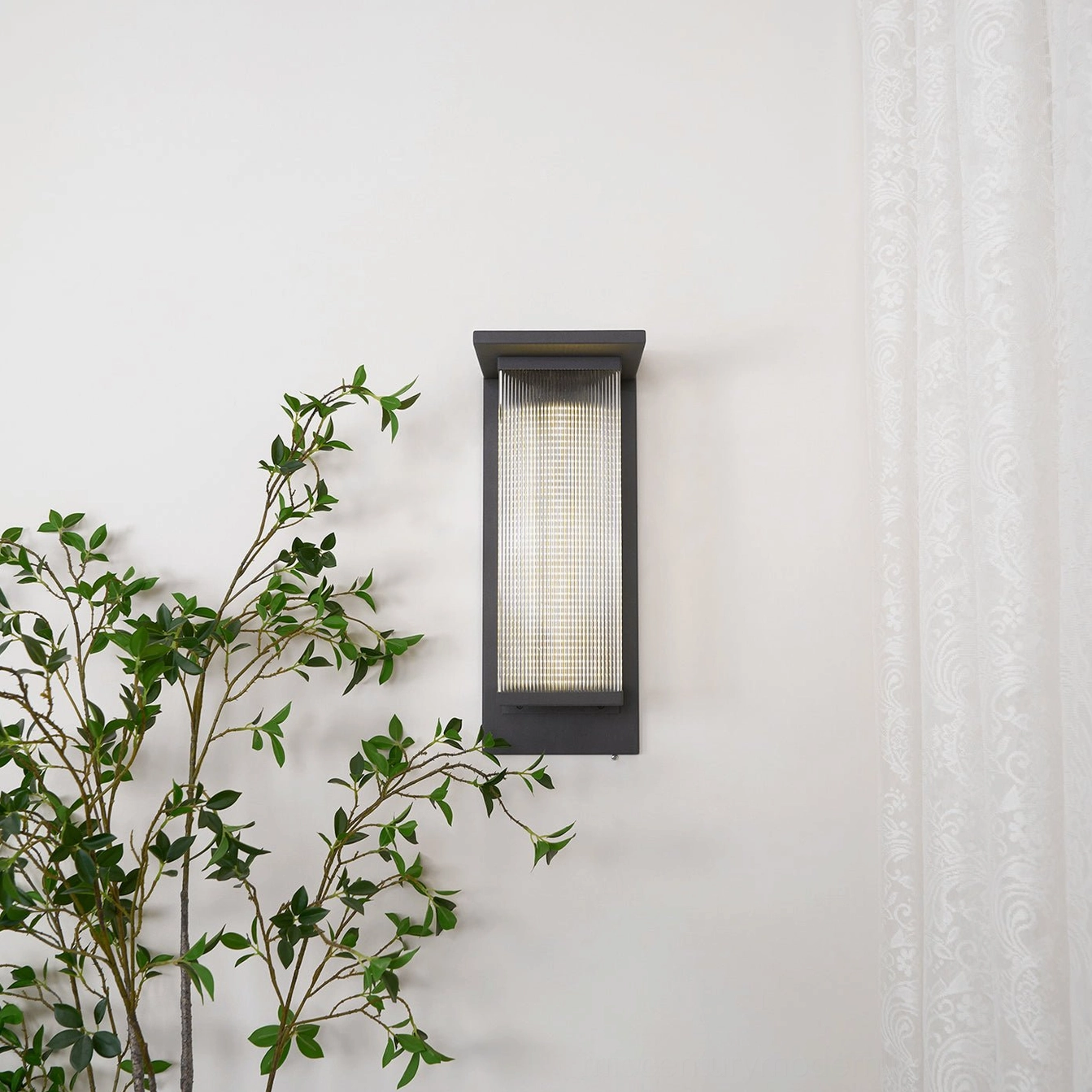 Oleron Box illuminated outdoor wall lamp, compact modern fixture, warm glow on wall, mid-century design aesthetic in natural setting