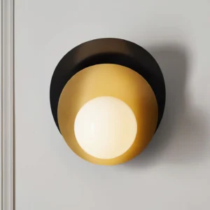 Illuminated Olivia wall sconce showing frosted white glass bulb glowing against layered black and brass metal framework