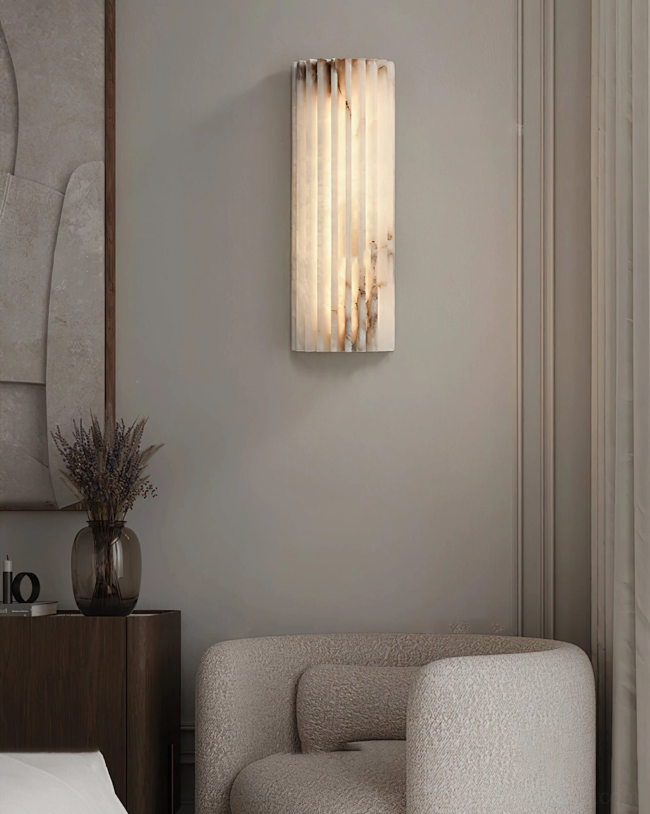 Illuminated Ondas alabaster wall sconce in minimalist modern lounge with neutral accent chair and dried flowers