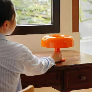 Orange mushroom table lamp on warm wooden desk with striped shirt detail, showing mid-century modern lamp in home interior setting