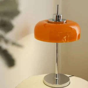 Retro orange glass table lamp positioned on home side table with foliage and neutral wall background