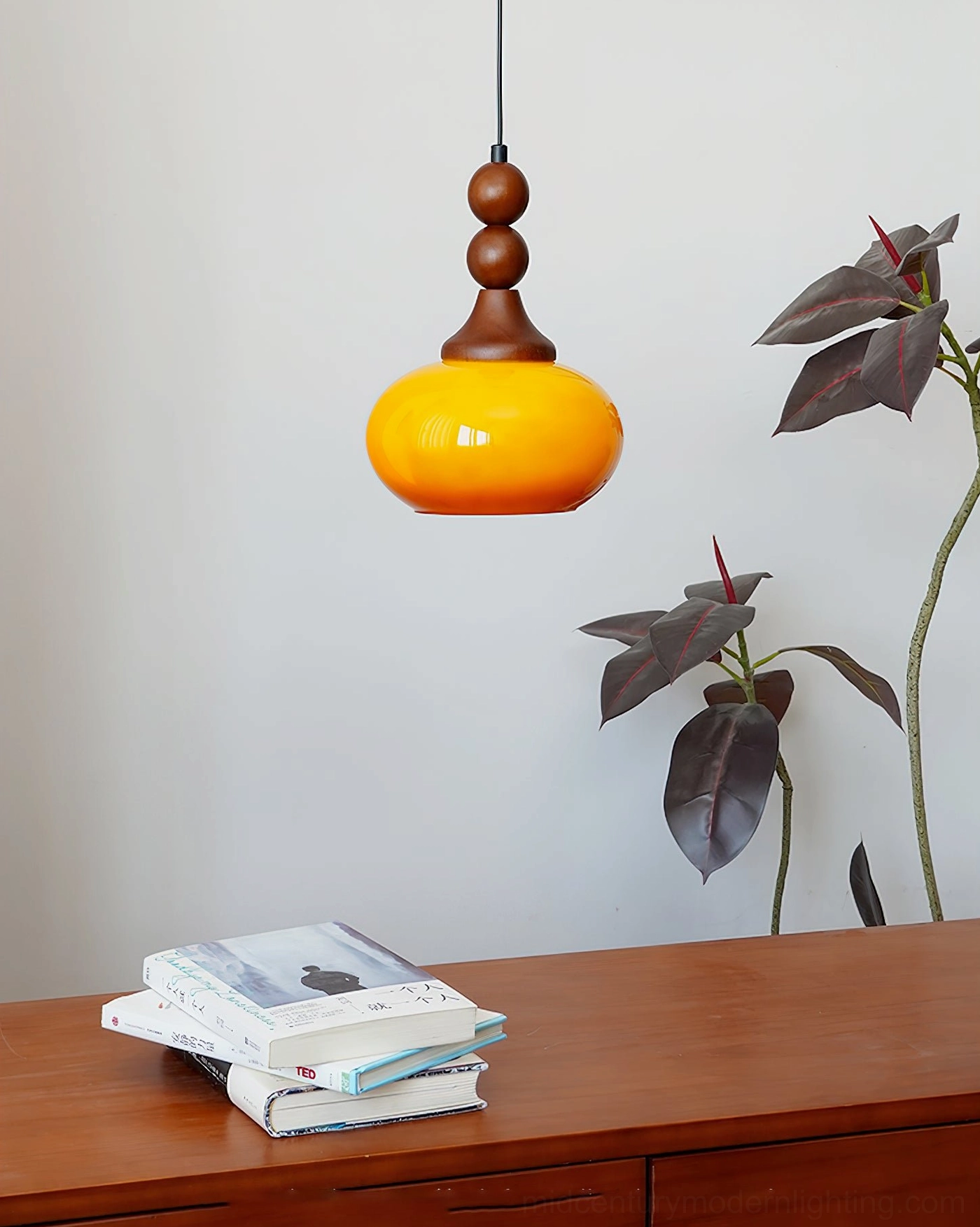 Orbique amber glass pendant light hanging over wooden dresser with foliage and botanical decor