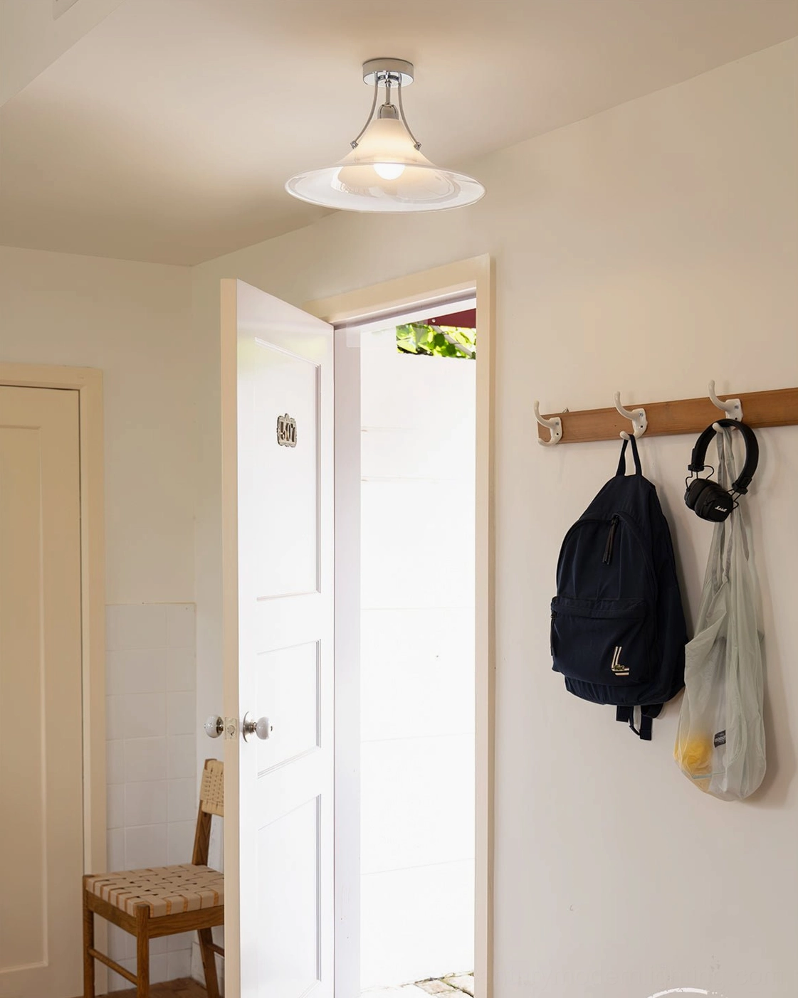 Orient ceiling light fixture in compact mudroom with wall coat hooks and warm neutral interior tones