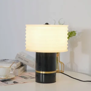 Illuminated Outela table lamp on desk with books and plants, warm ambient lighting in minimalist interior