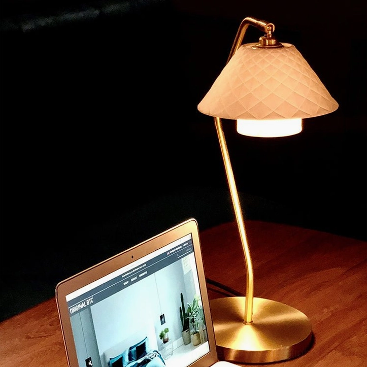 Oxford table lamp evening scene with beige quilted shade, warm glowing light on wood desk with laptop