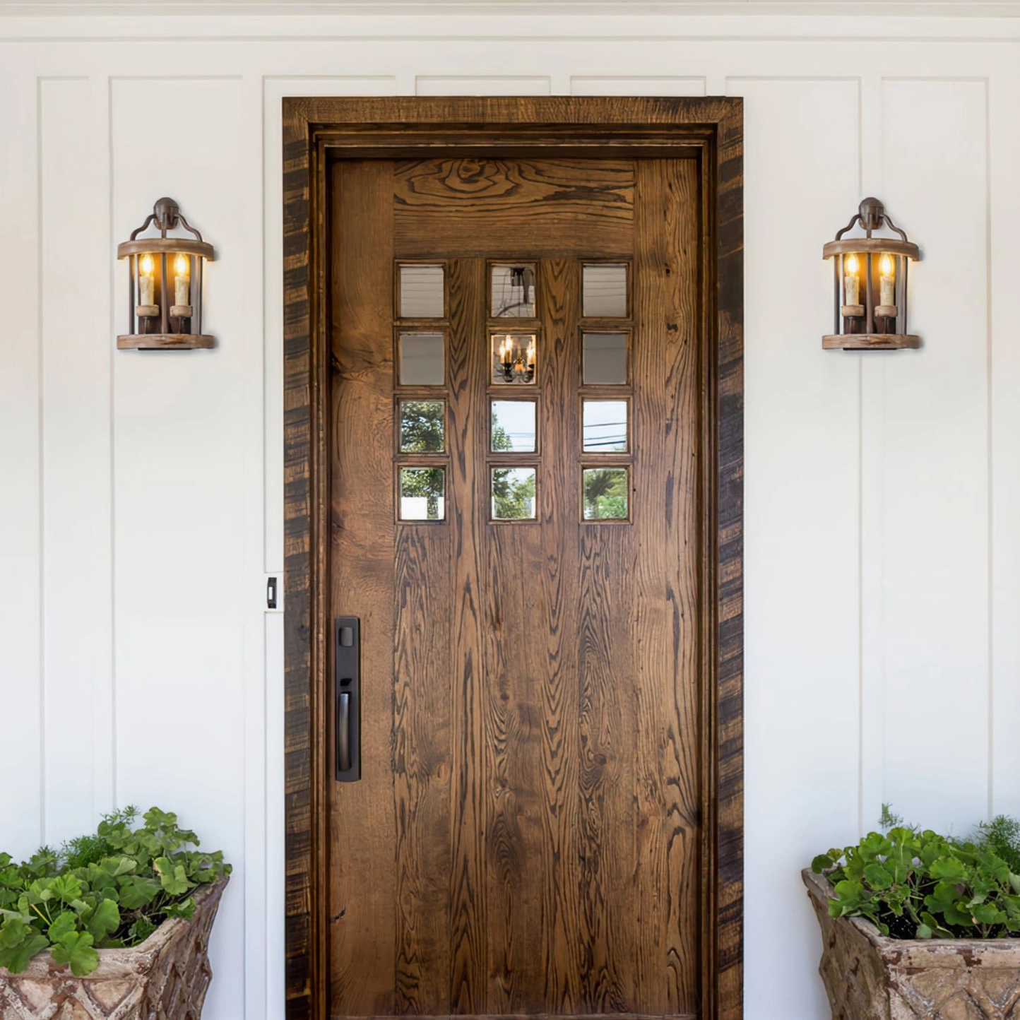 Matching pair of double candle wall sconces flanking wooden door in rustic farmhouse entry with planters