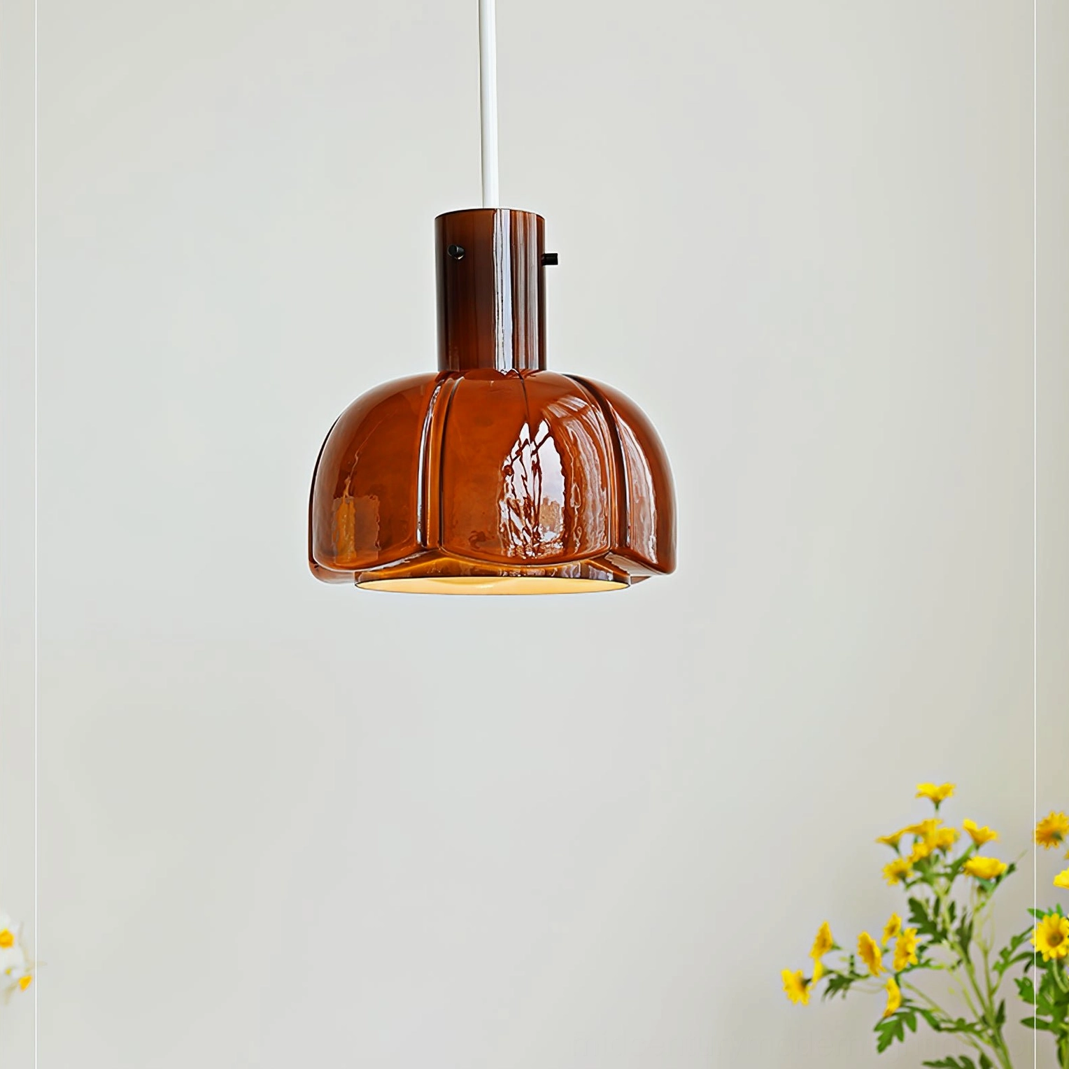 Glossy amber brown Paolina pendant light three-quarter view in space with yellow flower decorations