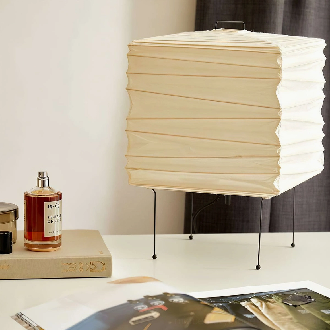 Contemporary handcrafted paper lamp styled on bedroom nightstand with decorative objects including perfume bottles and magazines, warm ambient lighting