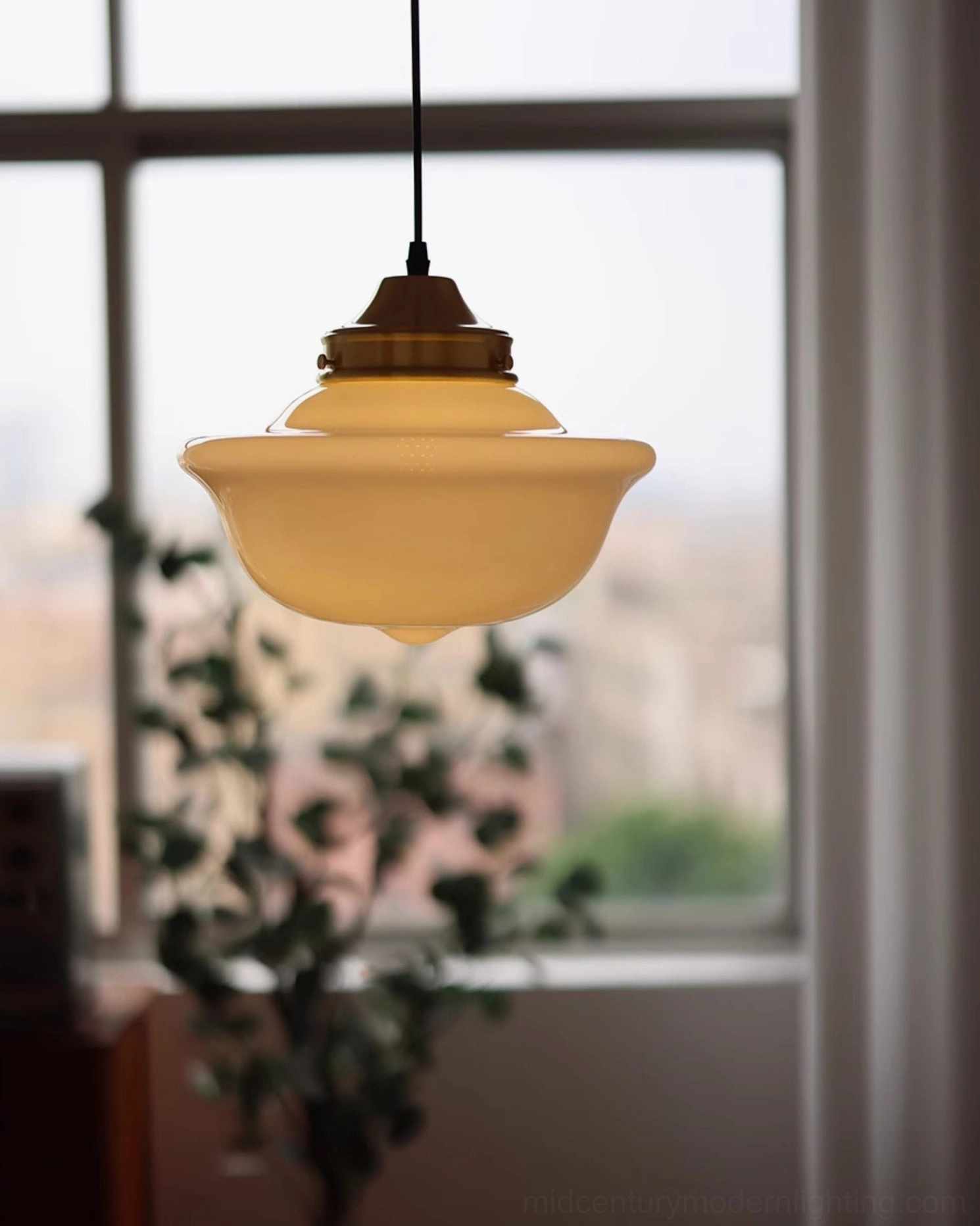 Pathson mid-century pendant light glowing by window in urban residential living space with plants