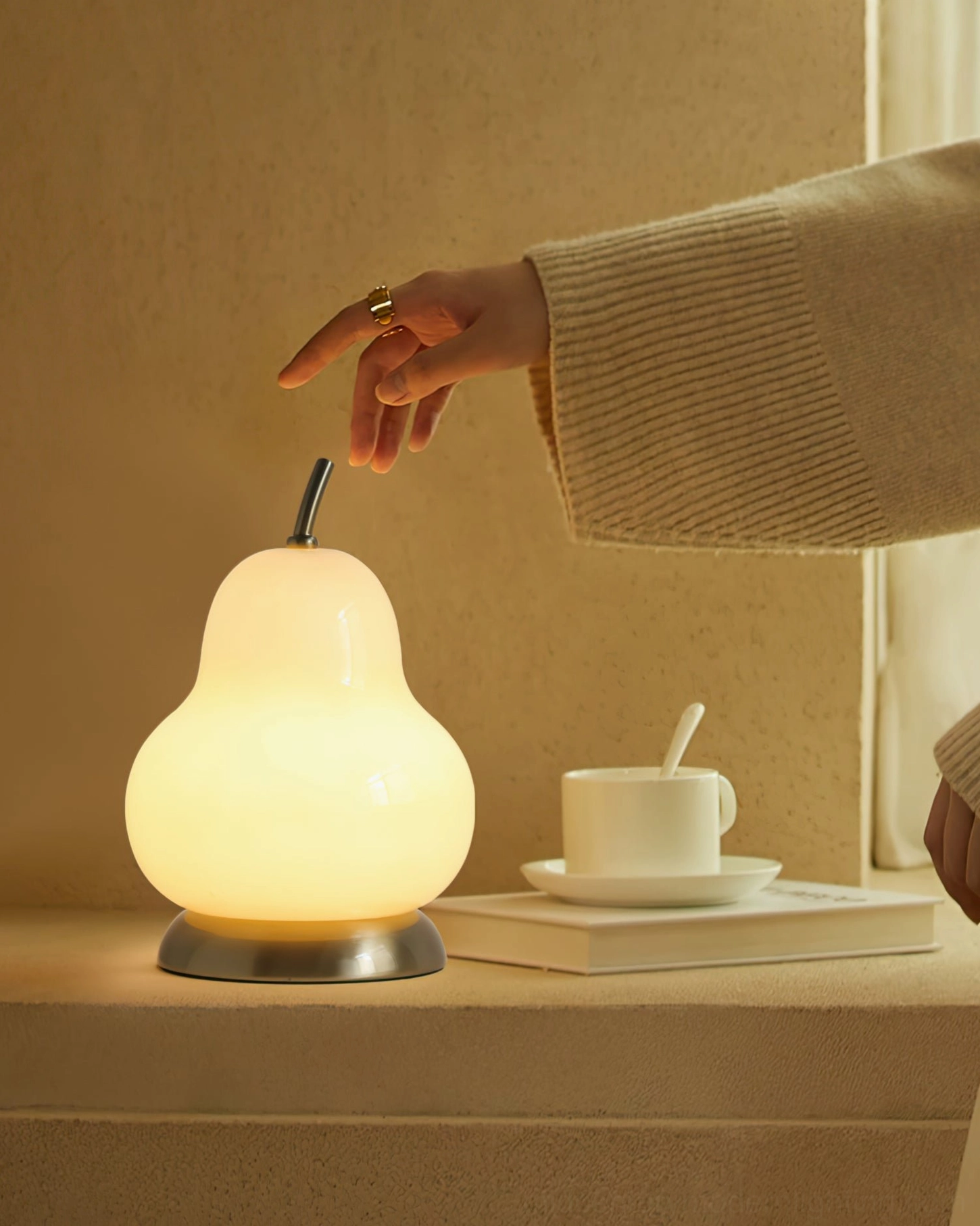 Close-up detail of cordless pear glass table lamp with hand model, showing warm LED light and textured base