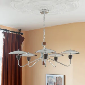 Peggy chrome chandelier illuminated in warm residential setting with brown curtains, demonstrating warm light ambiance and mid-century design aesthetic