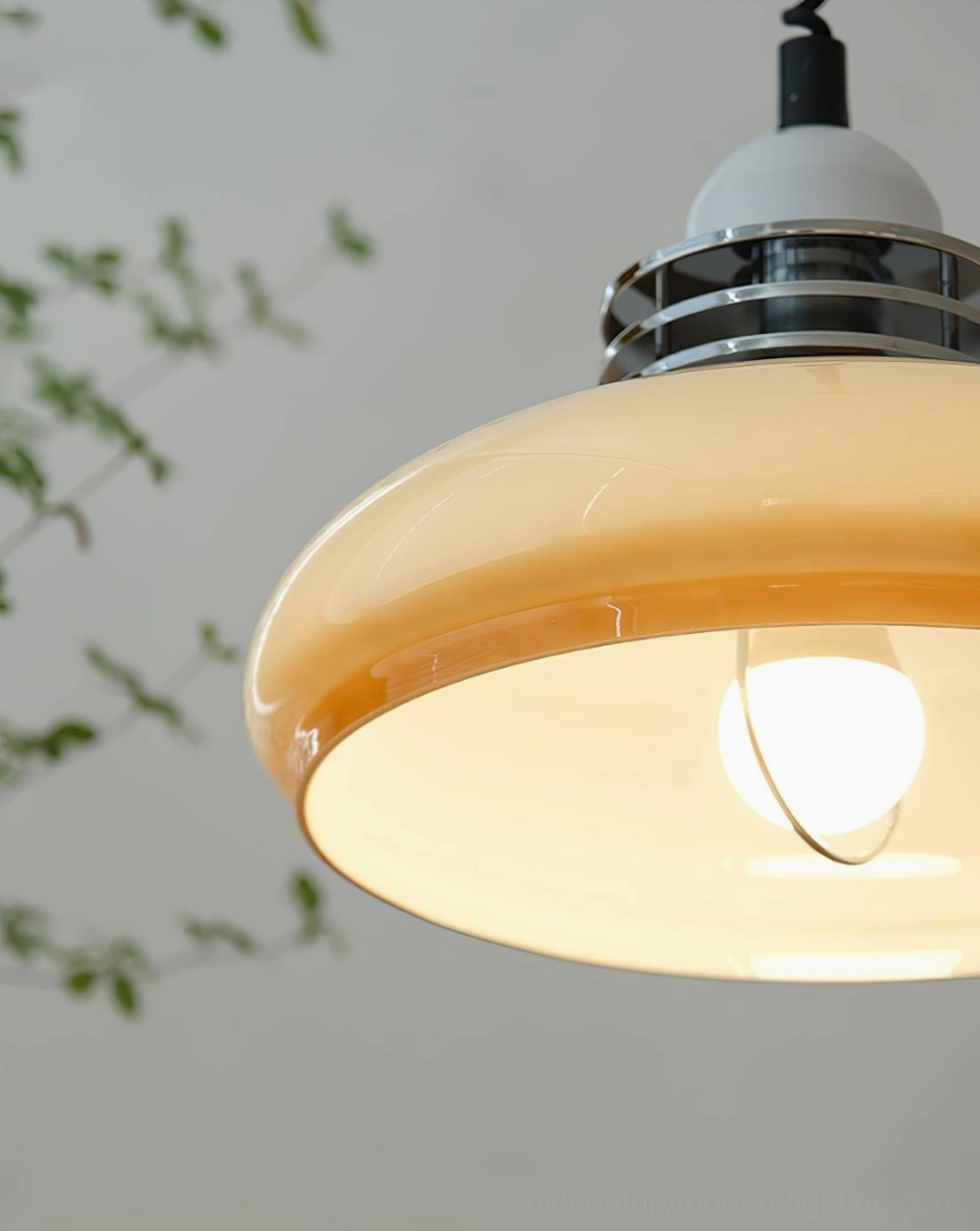Bottom view close-up of vintage pendant lamp showing glowing LED bulb inside gradient glass shade with foliage background