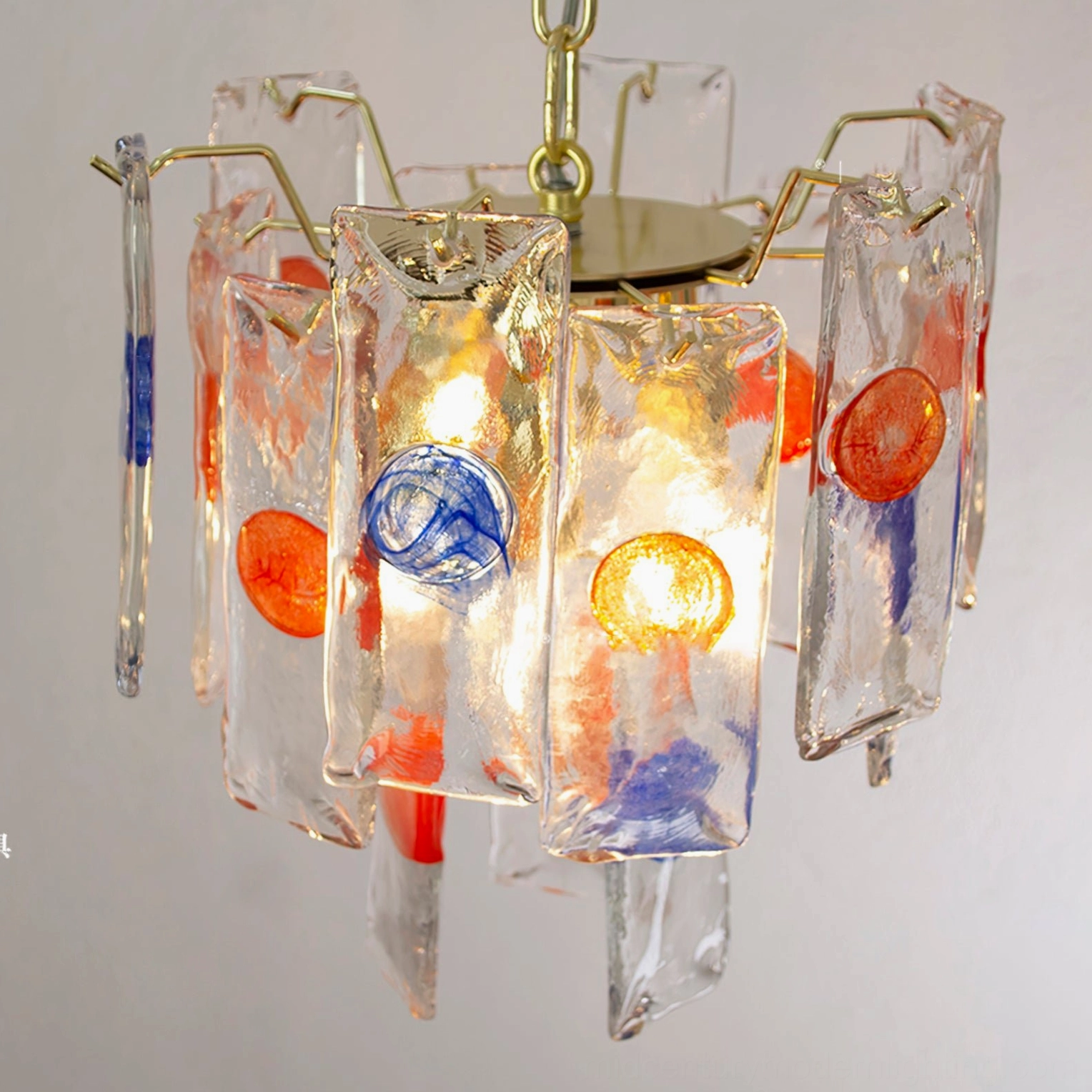 Low angle close-up of art glass pendant showing amber clear glass, gold metal frame with colorful glass decorations
