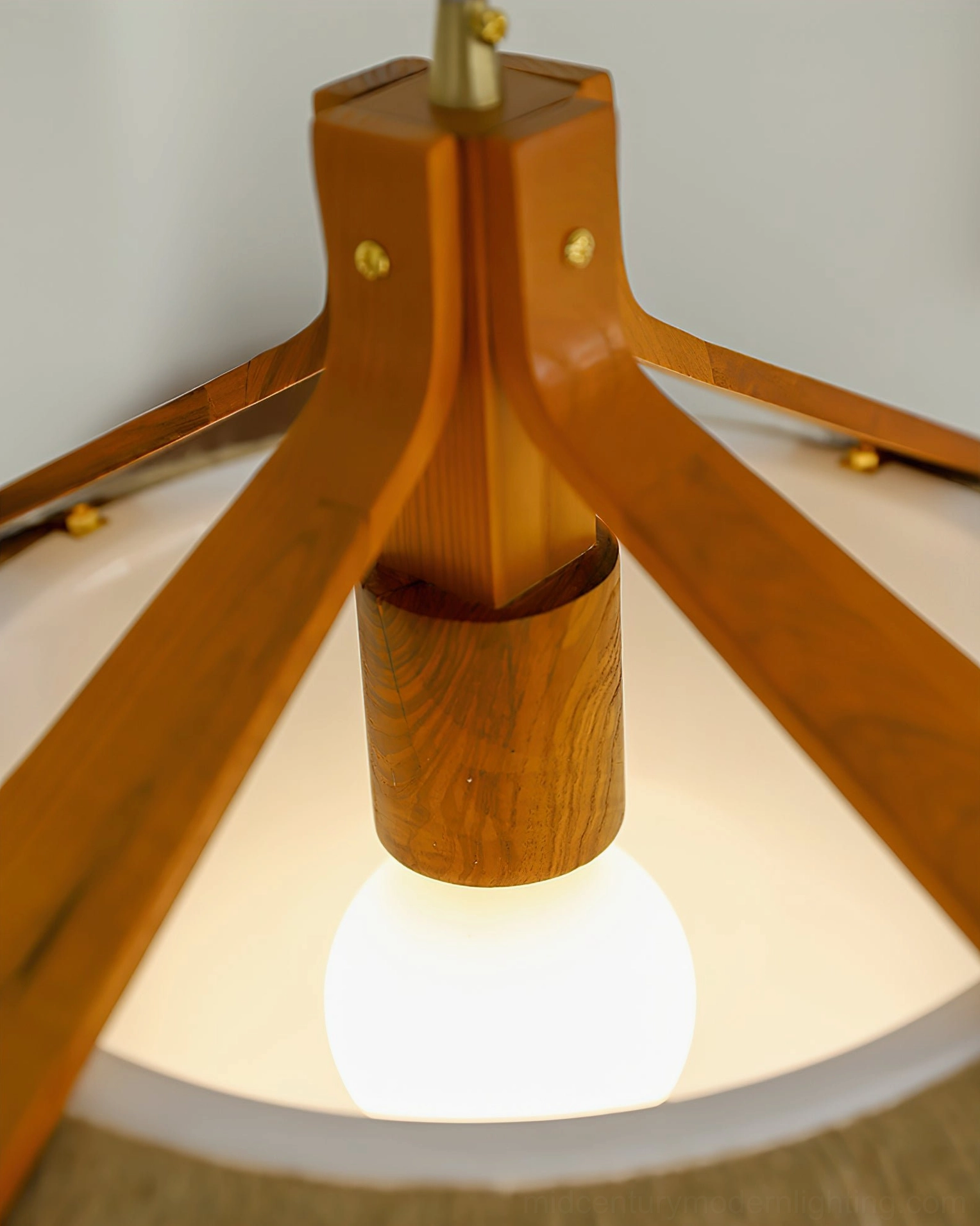 Bottom view close-up of pendant light joint showing wood grain texture, brass hardware fasteners, and warm Edison bulb interior illumination