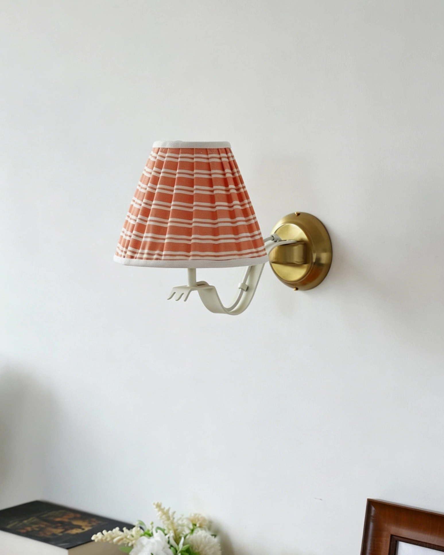 Penelope pleated wall sconce with curved brass arm creating sculptural modern silhouette on neutral wall