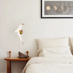 Perching Bird wall lamp installed in modern minimalist bedroom with white walls and brass accents, eye-level perspective