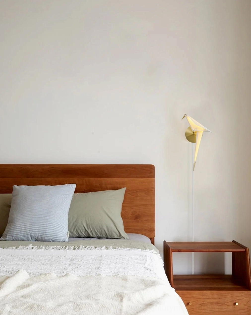 Perching Bird wall lamp in modern minimalist bedroom setting above wooden bed nightstand warm ambient lighting