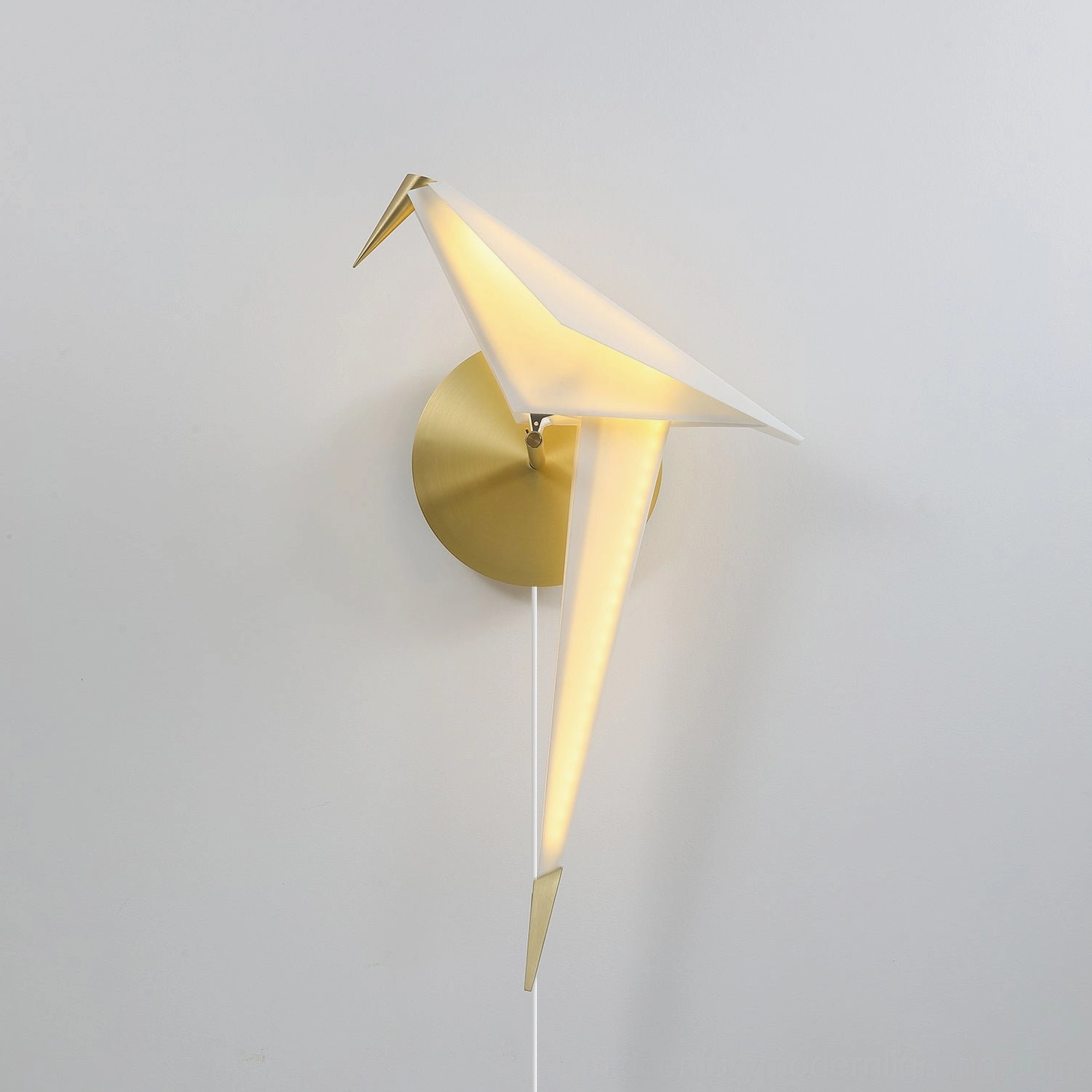 Illuminated origami bird wall lamp with brass gold mount on pure white wall left front angle warm glow