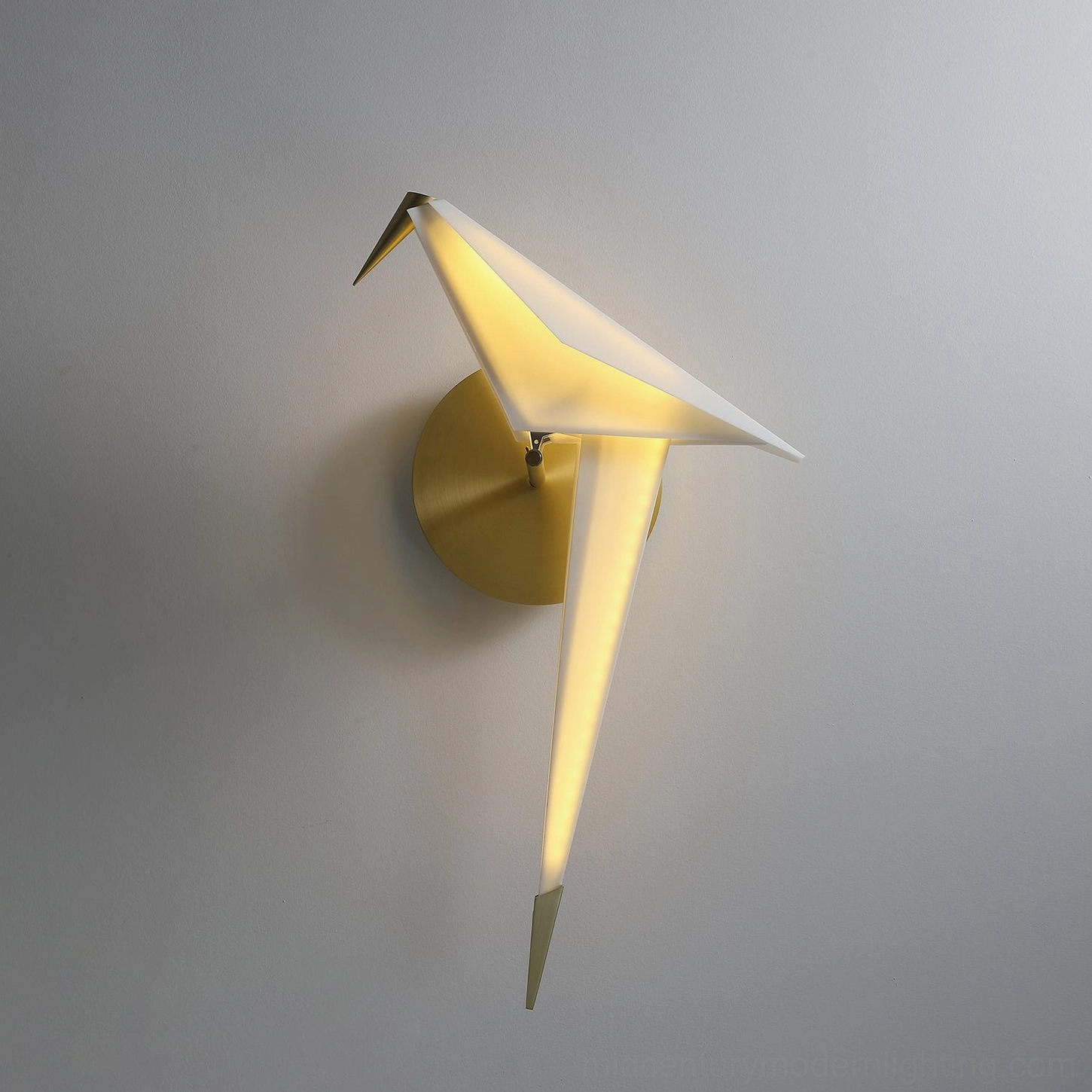 Low-angle front view of perching bird wall lamp with warm LED glow and brass gold mounting base on grey wall