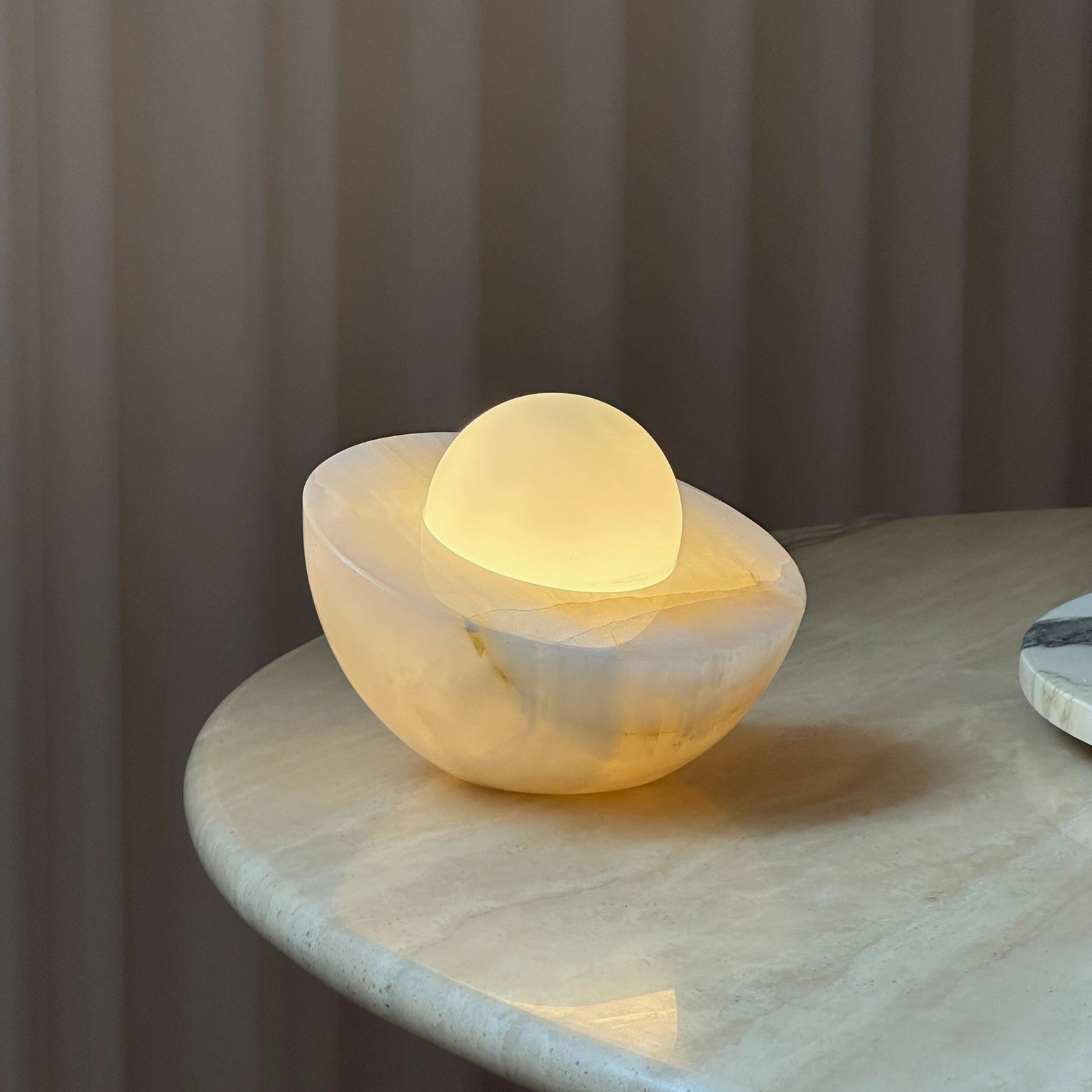 Piccola marble table lamp illuminated on marble side table, warm glowing ambient light emanating from frosted glass orb