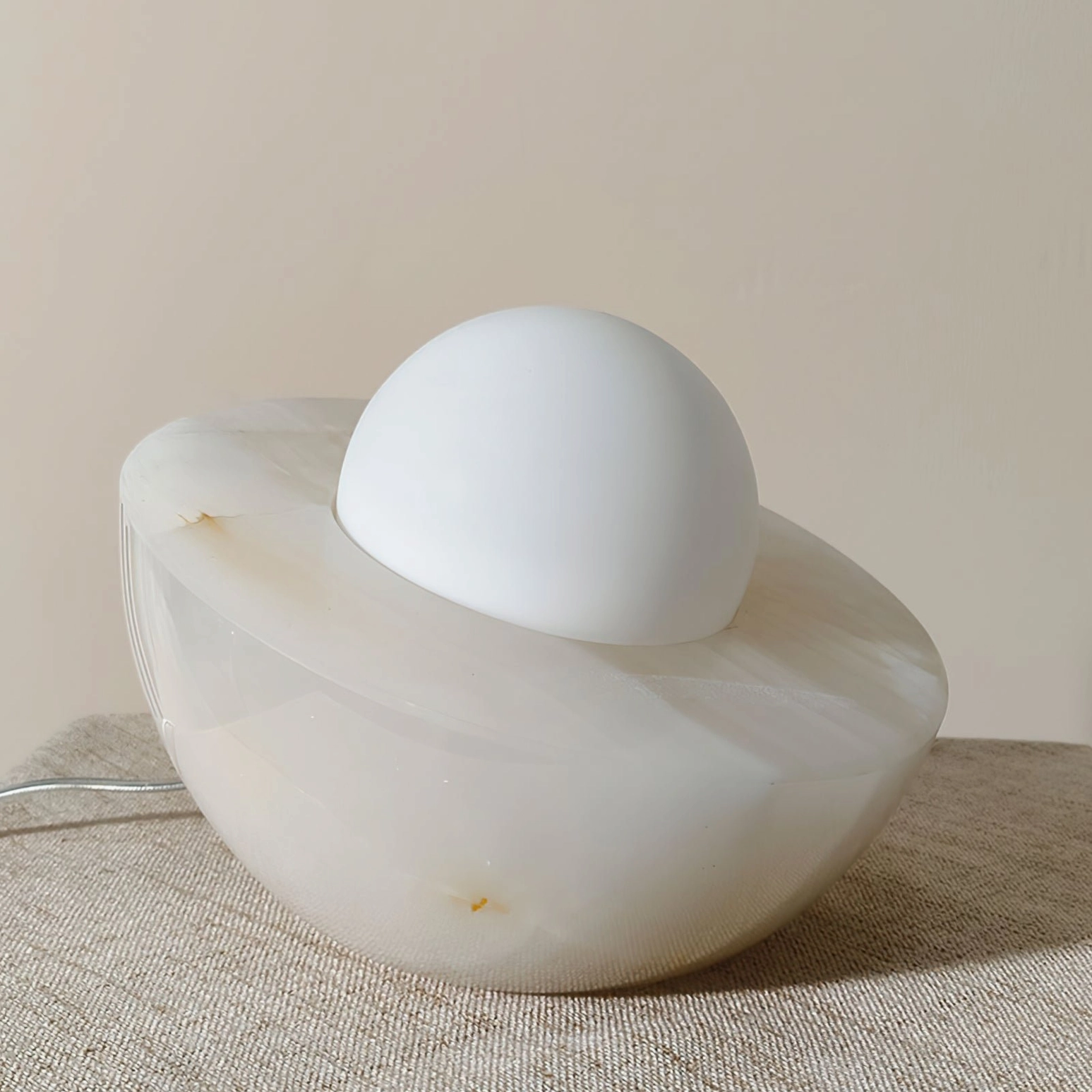Piccola marble orb lamp displayed on neutral linen fabric with minimalist home decor styling, side three-quarter angle