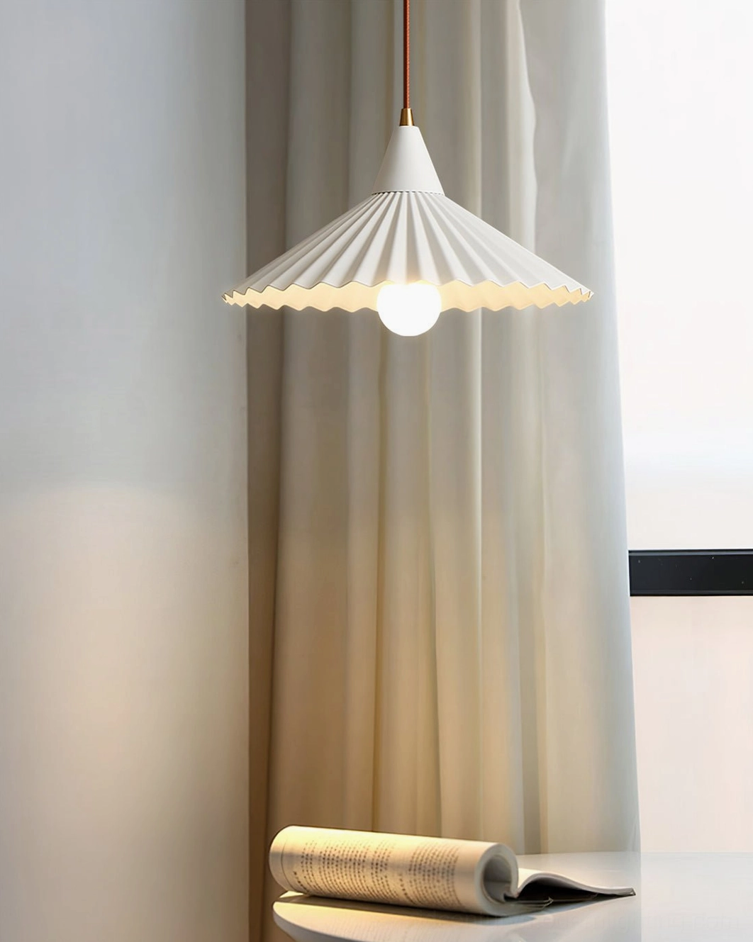 White Pieghe pendant light illuminating window-side home corner with sheer curtains and minimalist décor