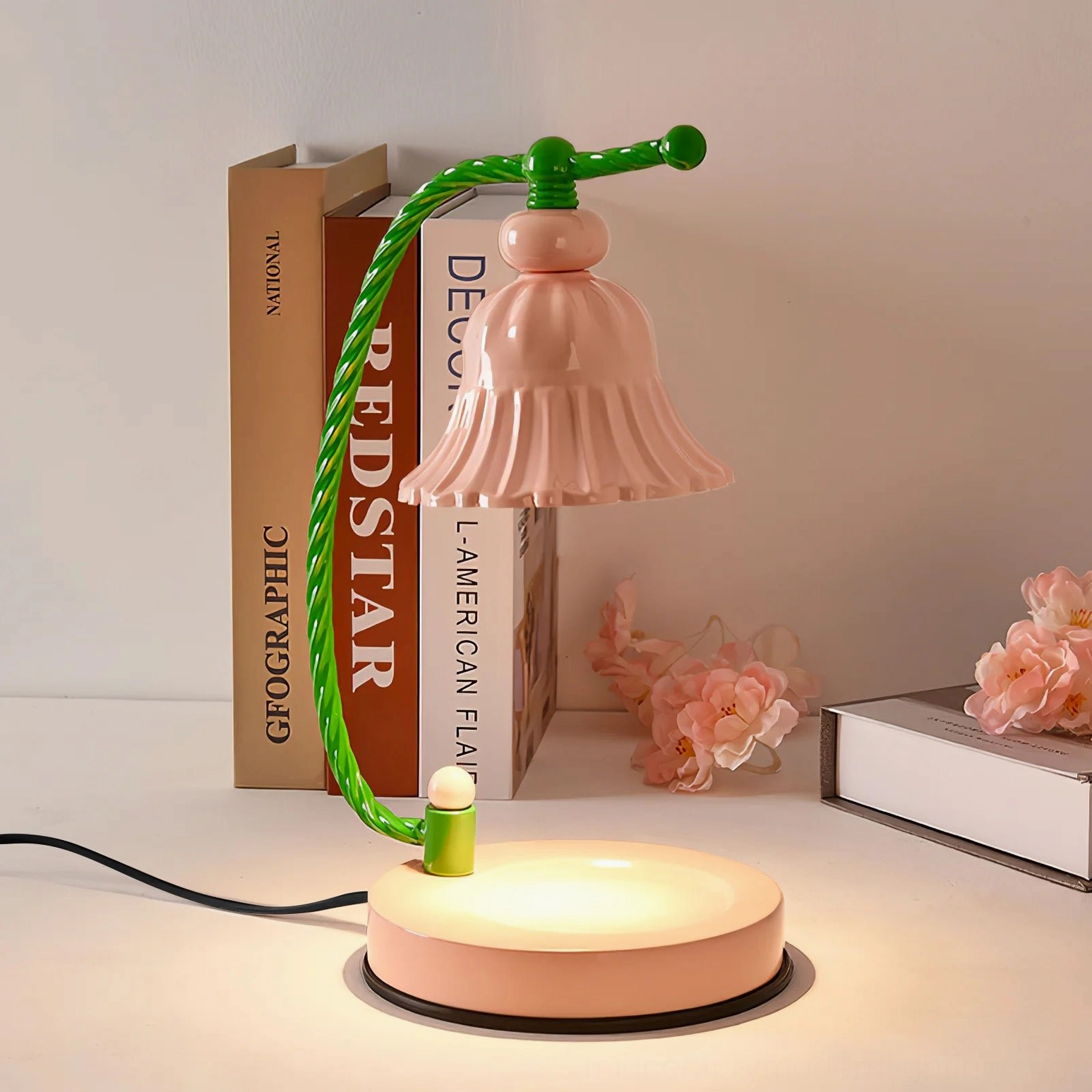Lit pink ceramic table lamp with warm glow on desktop with book decor and dried flower props
