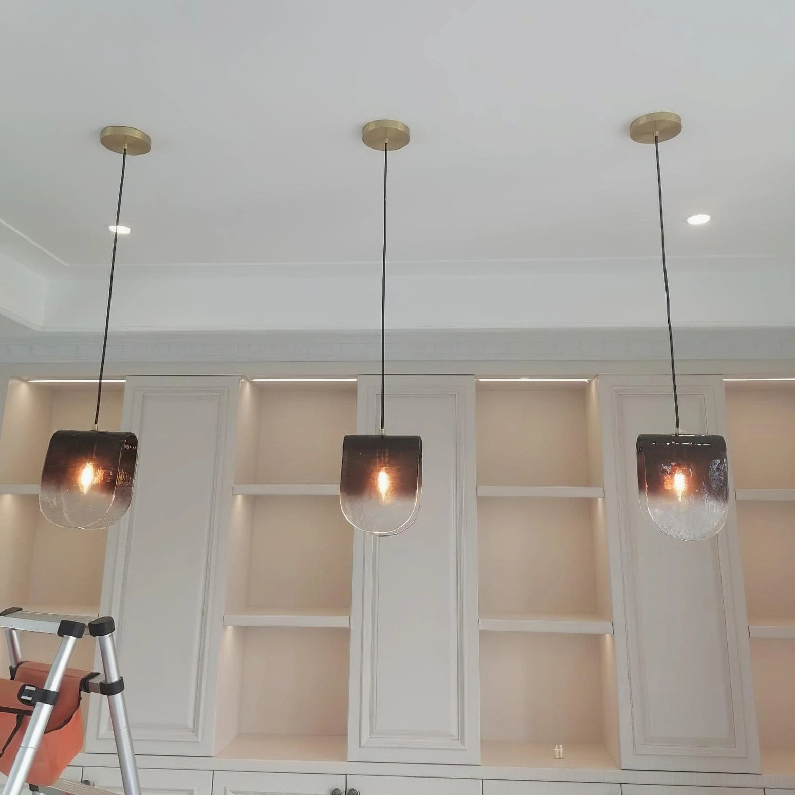 Three matching Planck pendant lights installed at staggered heights on modern ceiling with brass mounts