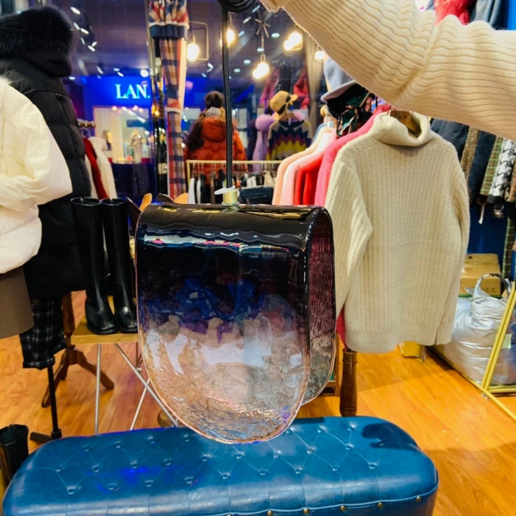 Planck pendant light displayed in modern retail clothing boutique on tufted bench