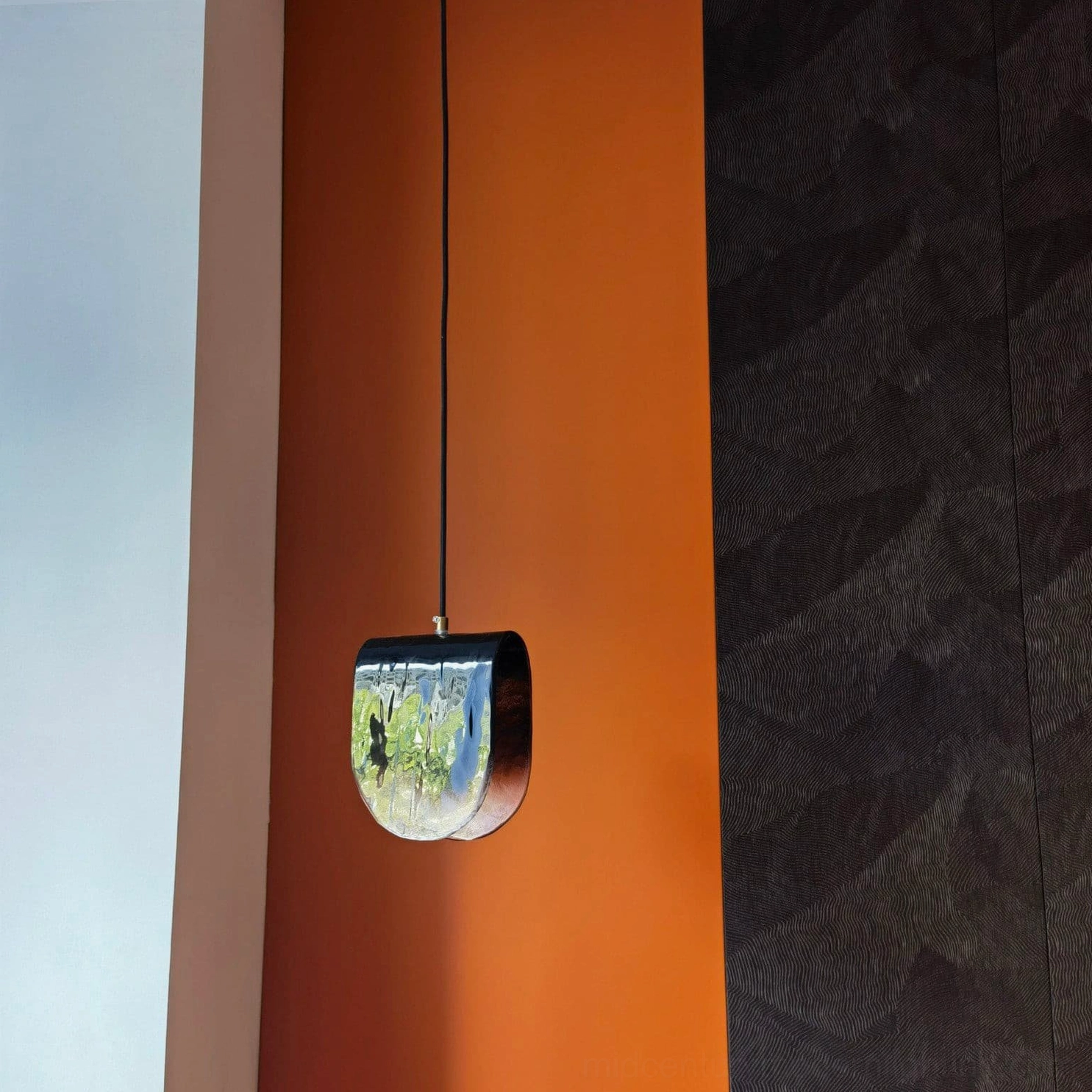 Single Planck pendant with black suspension cord hanging against dual-tone interior wall