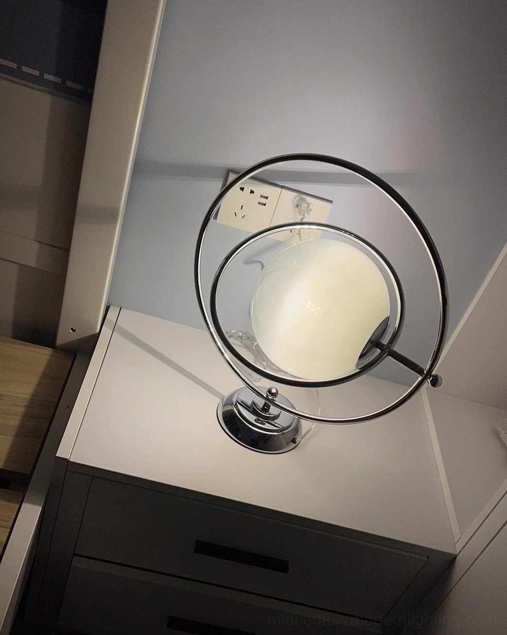 Space age planet lamp side view with black metal frame and matte silver base on dresser