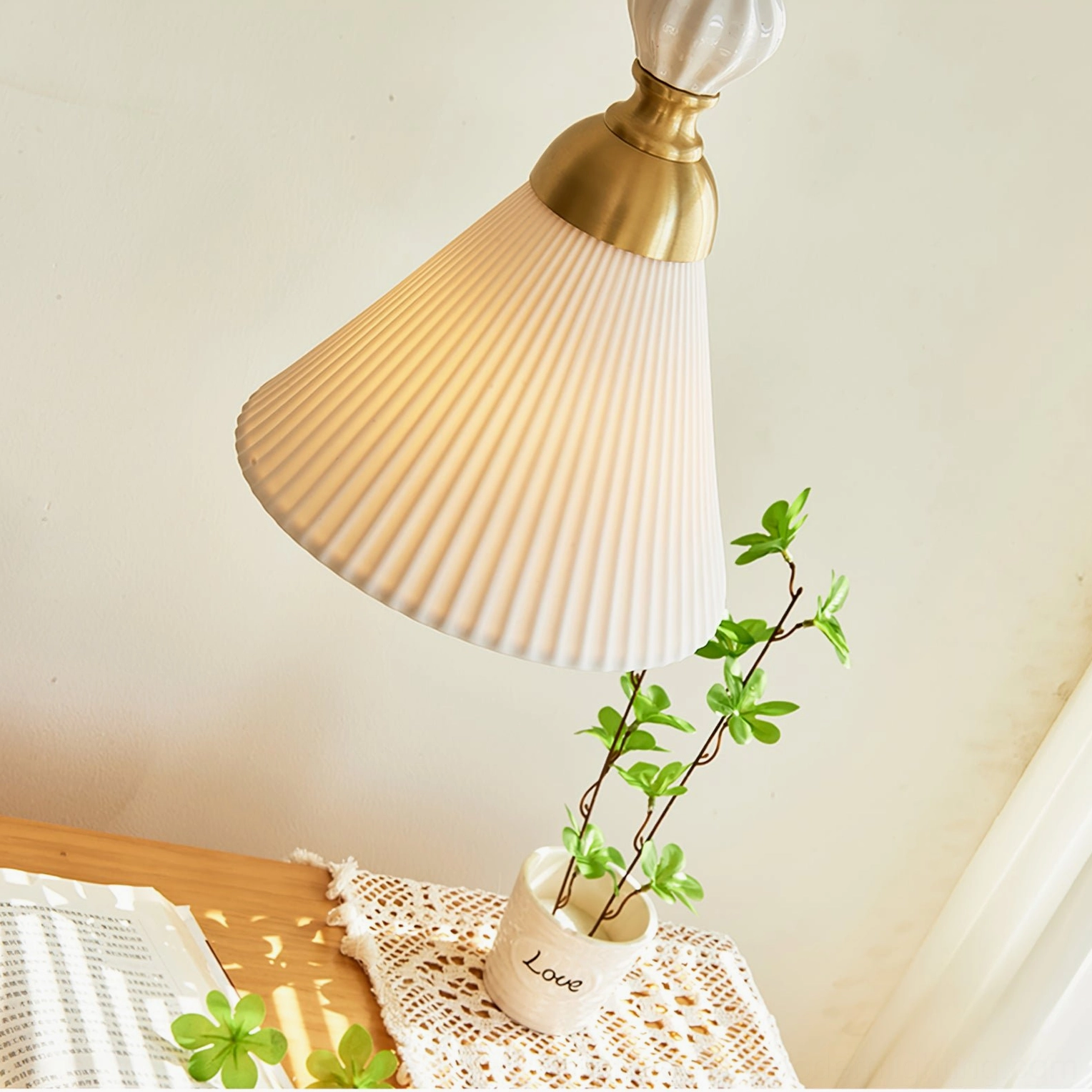 Pleated ceramic pendant light with warm glowing bulb above desk with potted plant decor