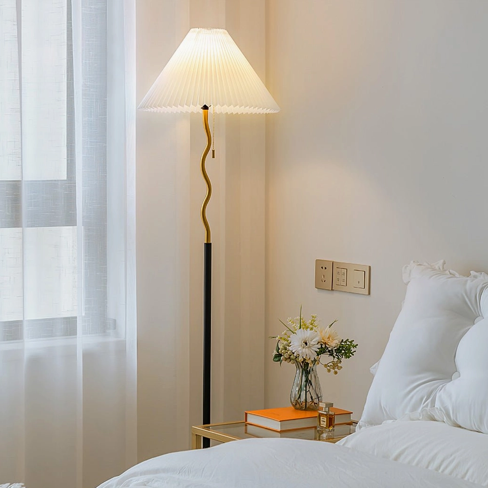 Bedroom side view of pleated floor lamp beside bed and nightstand with sheer window curtains