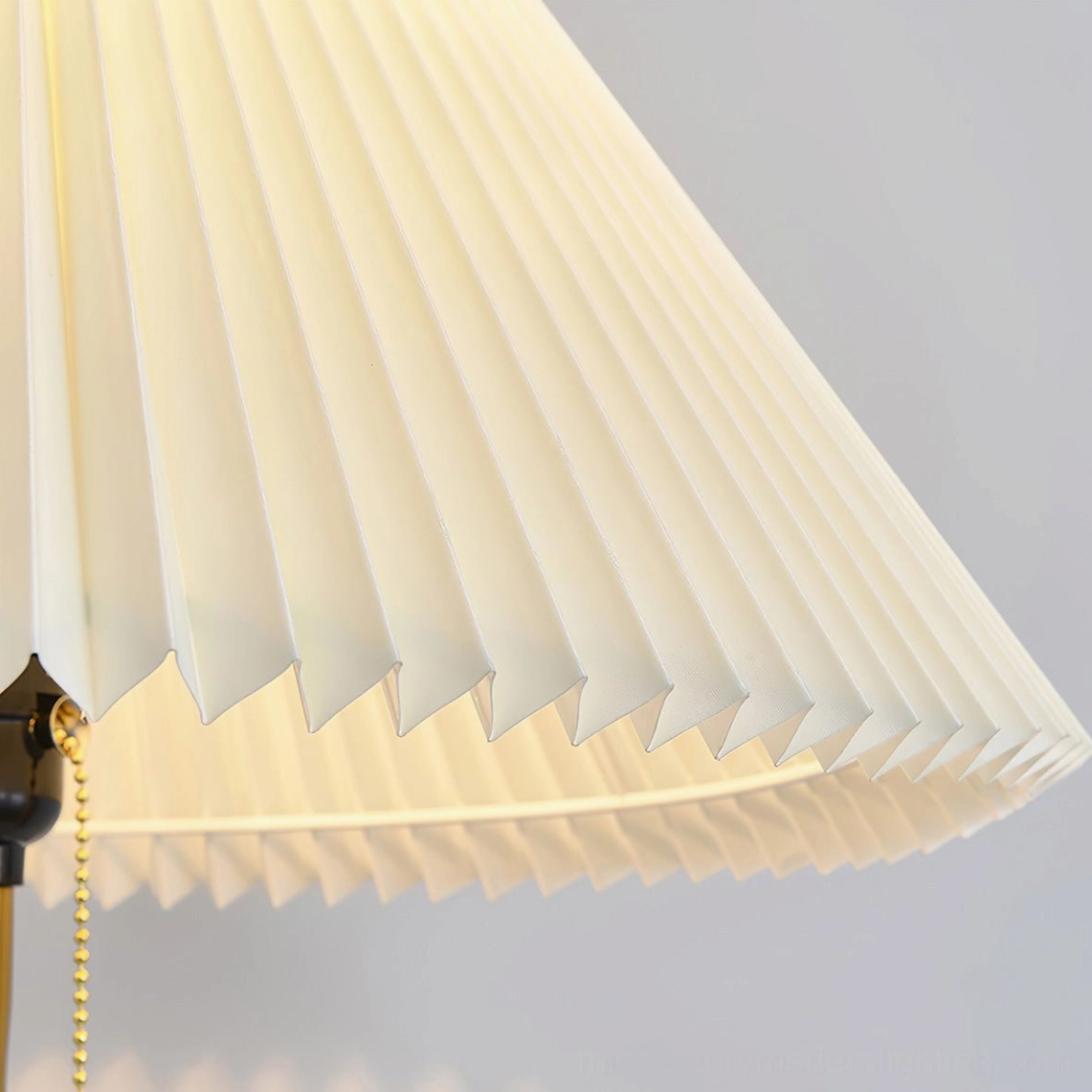Close-up detail of accordion-pleated white fabric shade with gold pull chain and metal hardware