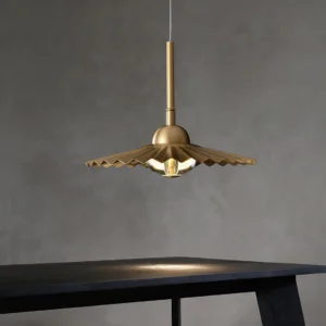 Single plié pendant light with matte brass finish and accordion pleats suspended in minimalist dark dining corner interior