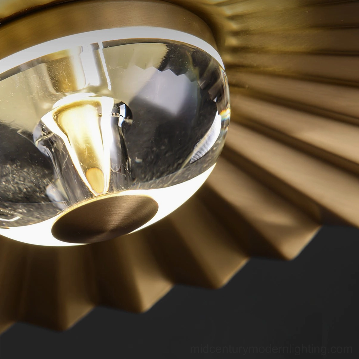 Close-up detail of plié pendant lamp fixture showing clear glass diffuser and polished brass pleated shade construction