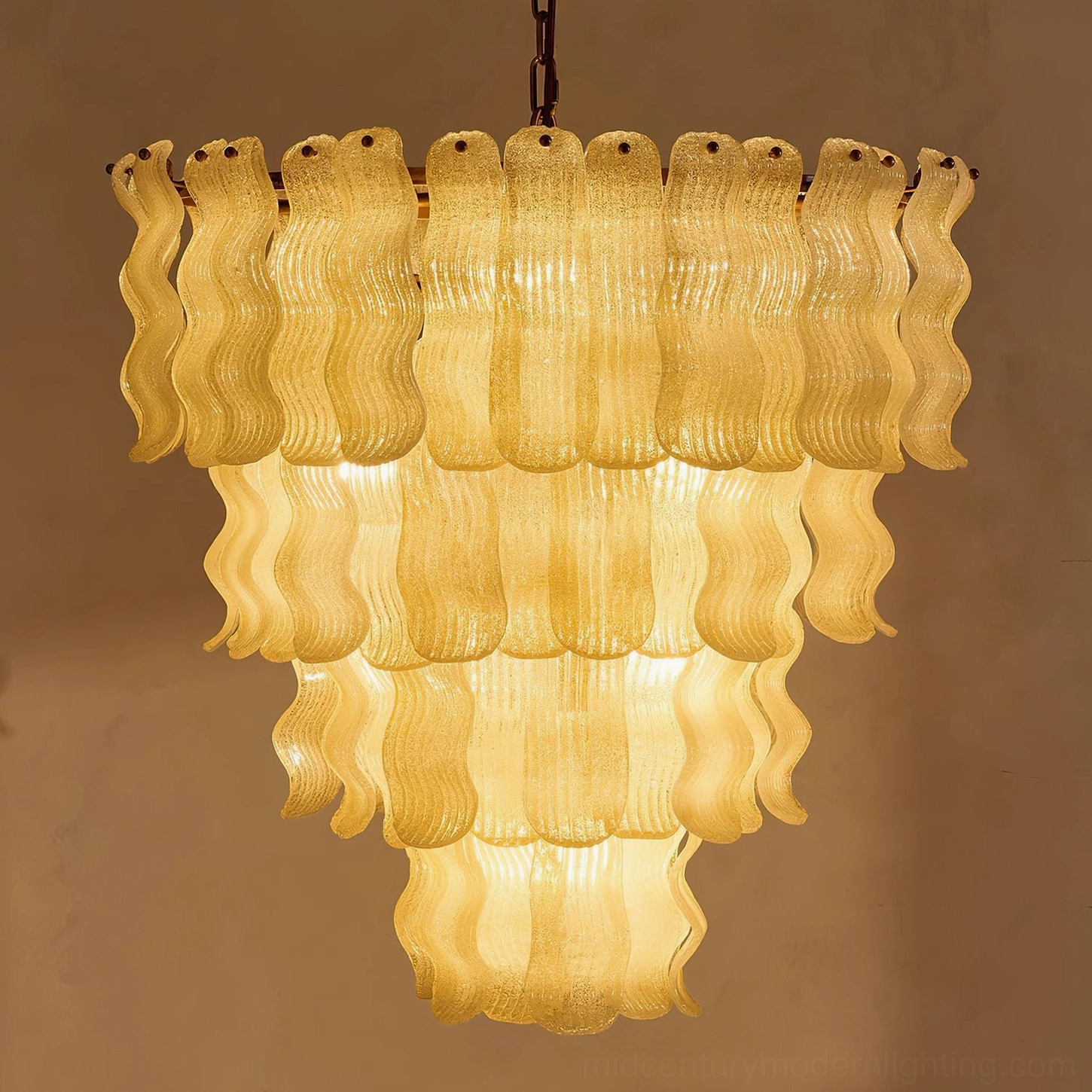 Illuminated Pollensa textured wave chandelier in warm glowing light showing amber ambiance and hand-poured glass luminosity
